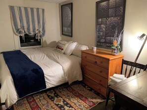 A bedroom with a bed, a dresser, a window with curtains, a rug, and a wall with a framed picture.