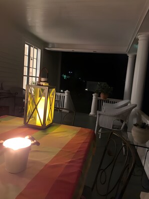 A balcony with a table, chairs, a lantern, and a view of the night sky.