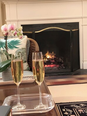 Une cheminée avec un feu de bois, deux coupes de champagne et un vase rempli d’orchidées sur une table.