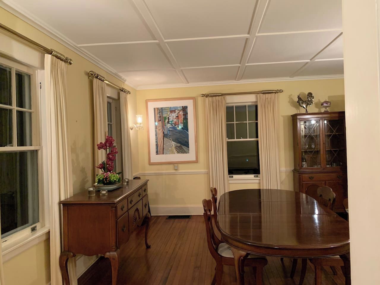A dining room with a wooden table and chairs, a cabinet, and a painting on the wall.