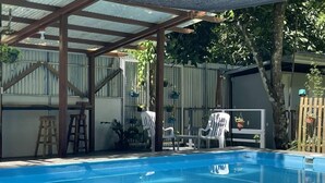 Zwembad met houten pergola, omgeven door potplanten en tuinmeubilair.