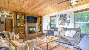 Un salon chaleureux avec une cheminée, des murs en bois et une grande fenêtre donnant sur la forêt.