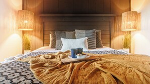 Une chambre confortable avec une tête de lit en bois, une literie à motifs et deux lampes de chevet.