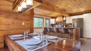 Un intérieur en bois comprenant une salle à manger avec une table dressée pour quatre personnes, un coin cuisine et de grandes fenêtres.