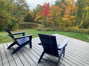 A wooden deck with two Adirondack chairs facing a pond surrounded by autumn-colored trees. - Not-so-tiny, Tranquil, Pond Front Bungalow (Canaan)