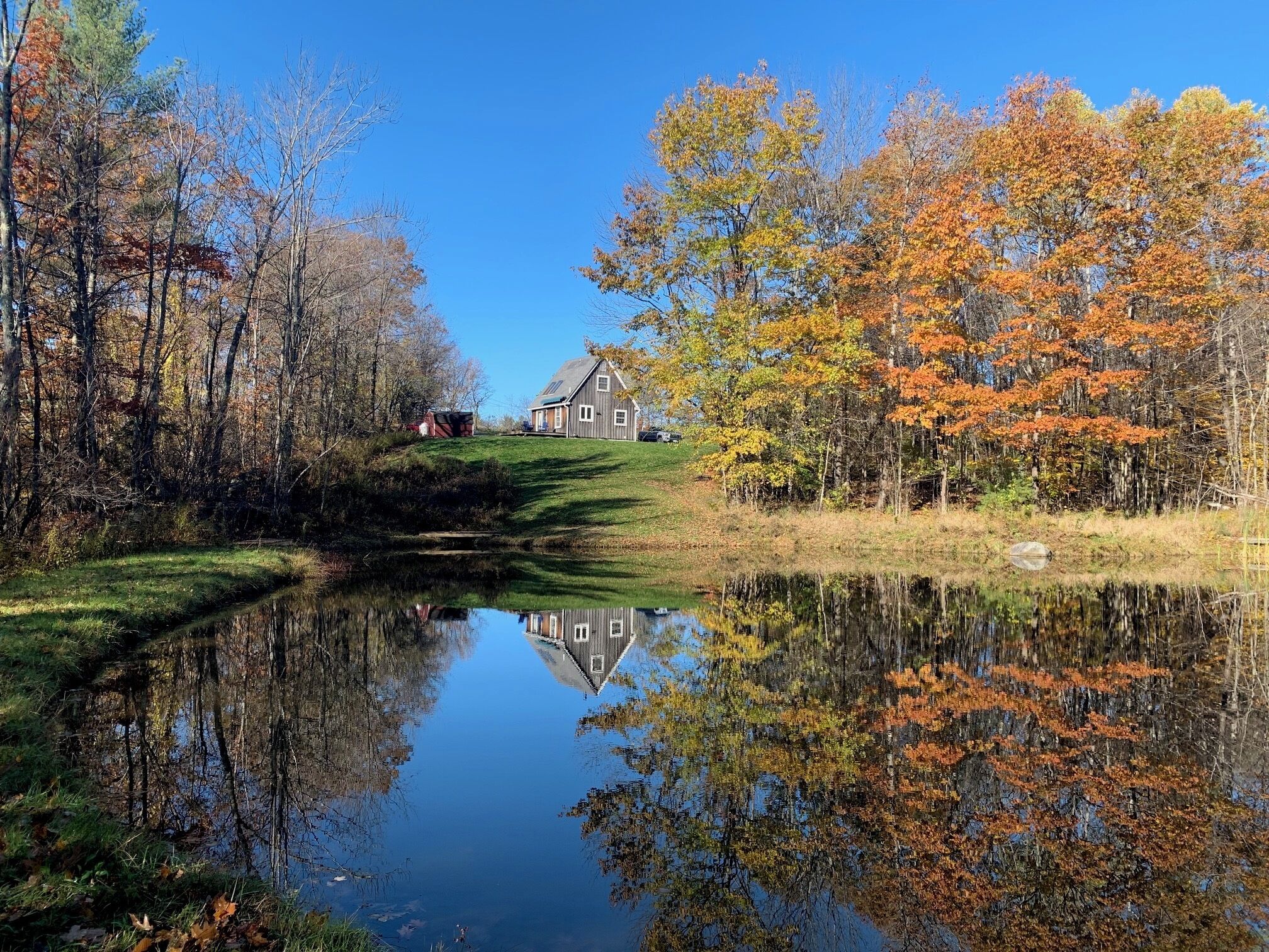 A house with a pond in front, surrounded by autumn-colored trees.