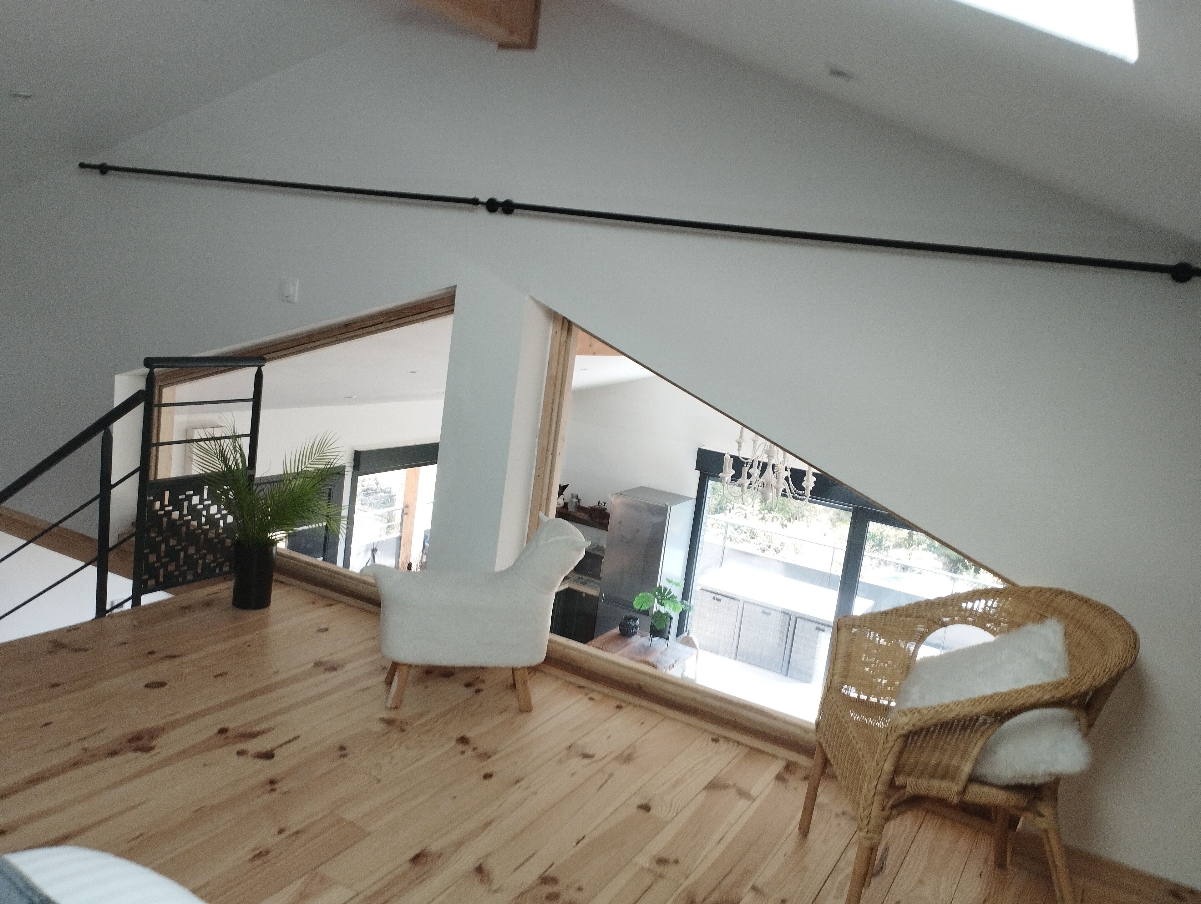 A spacious loft with a high ceiling, wooden flooring, a staircase, and a large window offering a view of the outdoors.