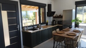 A modern kitchen with dark cabinetry, a large island with stools, a built-in oven, and a view through the window.