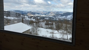 A room with a large window offering a view of a snowy landscape with mountains and trees.