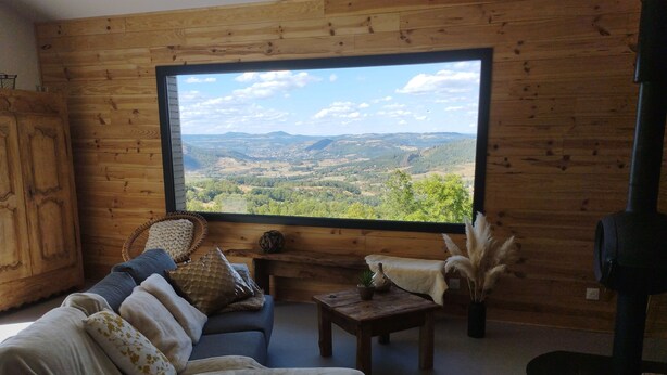 A cozy room with a large window, wooden walls, a sofa, a small table, and a cowhide rug.