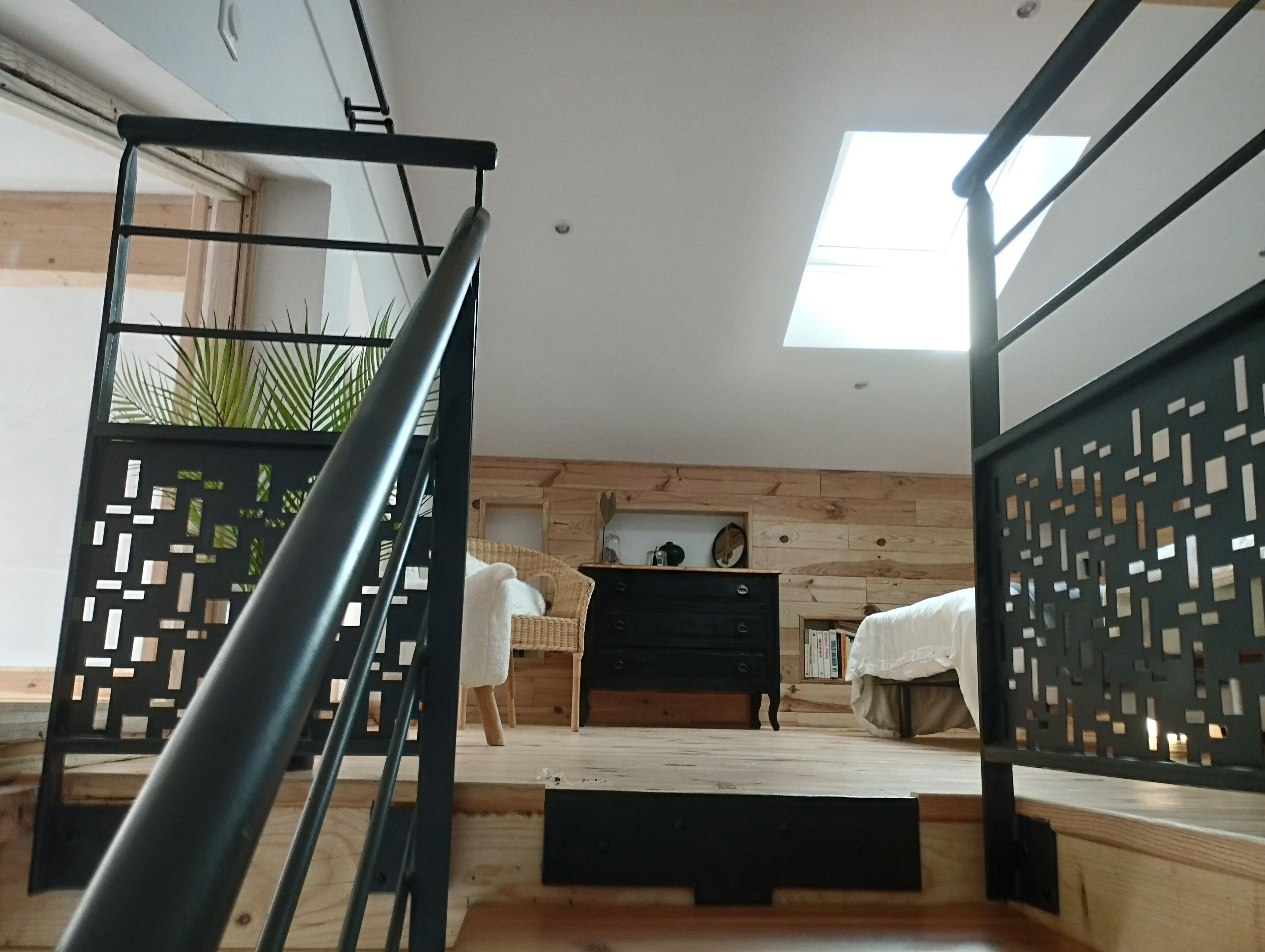 A modern interior with a staircase, wooden flooring, a black-framed window, and a ceiling with a skylight.