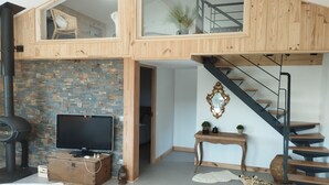 A loft-style living space with a stone wall, a television, a wooden chest, a staircase, and a rustic decor.