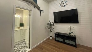 Una sala de estar moderna con un pez vela montado en la pared, una brújula decorativa, un televisor de pantalla plana, un mueble de entretenimiento negro y una planta en maceta.