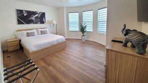 Un dormitorio moderno con una cama de madera, una mesita de noche, una lámpara de pie y un ventanal con persianas.