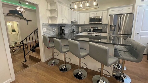 Una cocina moderna con una isla central, taburetes de bar, electrodomésticos de acero inoxidable y una escalera que sube a un nivel superior.