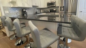 Una cocina moderna con armarios blancos, un refrigerador de acero inoxidable, un microondas integrado y una isla grande con taburetes de bar.