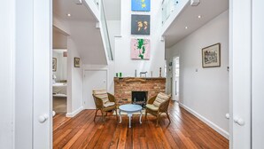 Amplia habitación con piso de madera, una chimenea, dos sillones de mimbre, una mesa redonda y una escalera que conduce a un nivel superior.