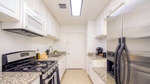 A kitchen with white cabinets, a stainless steel refrigerator, a stove, and a microwave.