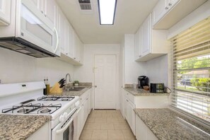 Kitchen features a gas stove, range hood, and small window with blinds.