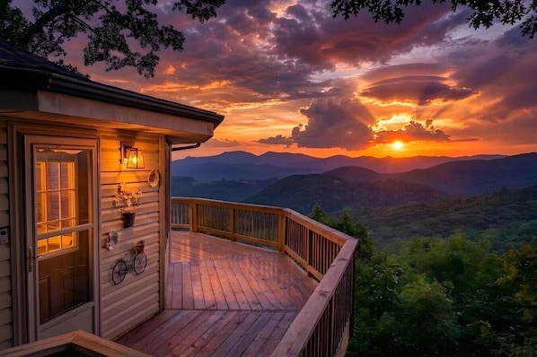 A wooden deck with a view of mountains and a sunset.