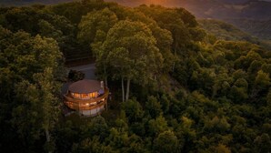 A circular building surrounded by dense forest, with a road leading to it.