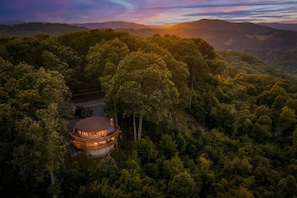 A circular building surrounded by dense forest, with a road leading to it.