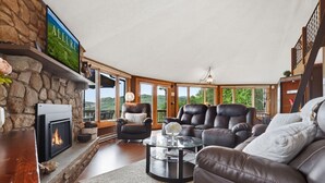 A cozy living room with a fireplace, leather sofas, a glass coffee table, and a stone wall.