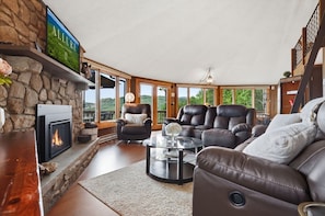 A cozy living room with a fireplace, leather sofas, a glass coffee table, and a stone wall.