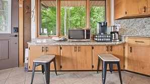 A kitchen with wooden cabinets, a microwave, a coffee maker, and a window with a view of trees.