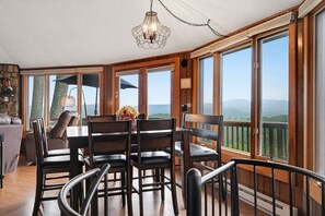 A dining area with a table and chairs, large windows with a view, and a chandelier.