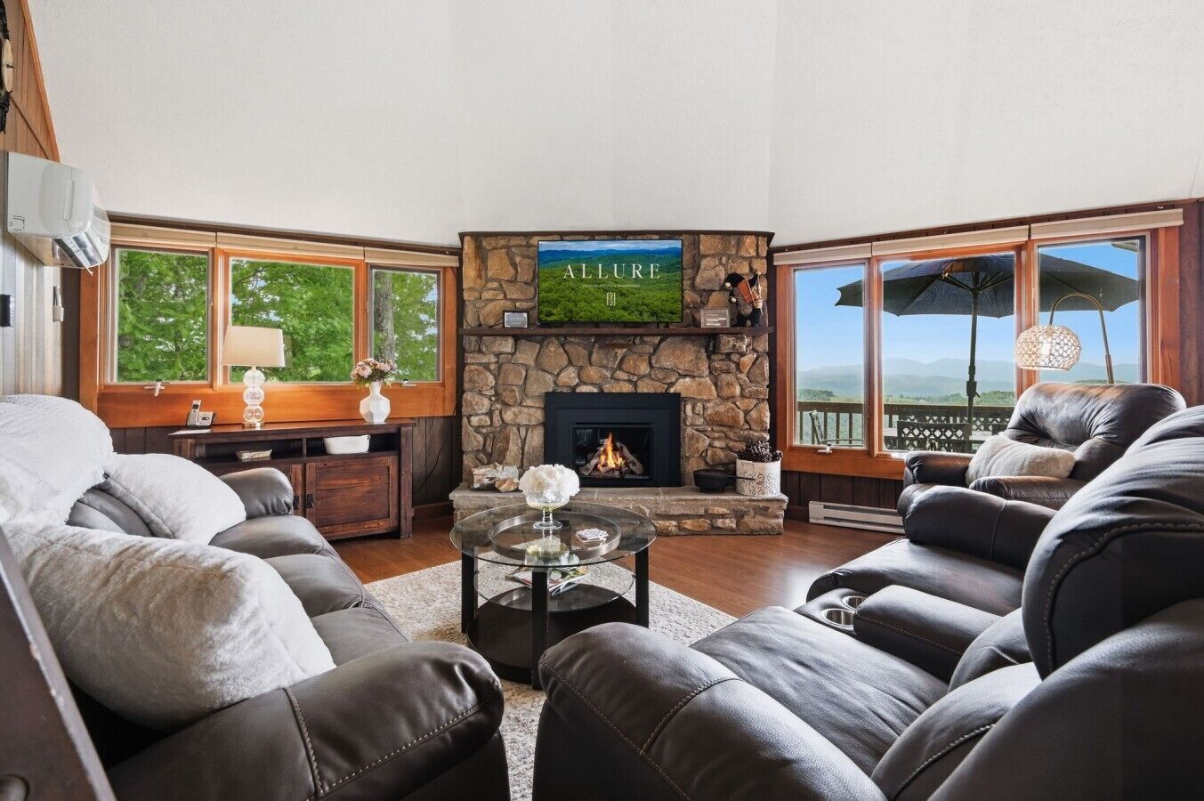 Un salón con chimenea de piedra, sofás de cuero, una mesa de centro de cristal y un amplio ventanal con vistas.