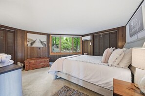 Quarto com uma cama grande, paredes de painel de madeira, janela com vista, um banco e uma pilha de toalhas.