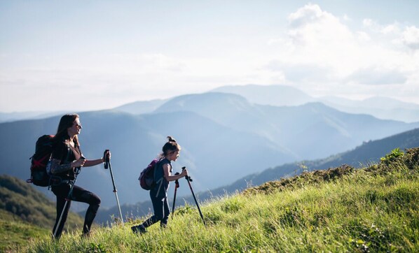 Twee wandelaars op een grasheuvel, met een bergachtig landschap op de achtergrond.