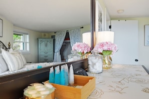 A bedroom with a large mirror, a wooden headboard, a bedside table with toiletries, and a window with curtains.