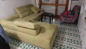 Una sala de estar con un sofá, una mesita, un sillón colorido y un suelo estampado.