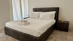 Een net opgemaakt bed met een donker hoofdbord, witte beddengoed en een nachtkastje met een lamp.