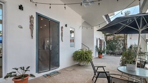 Un patio al aire libre con puerta de vidrio, plantas en macetas y una mesa redonda con sillas.