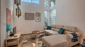 Una sala de estar con un sofá a rayas, un televisor sobre un mueble de madera, una mesita redonda y una alfombra mullida.