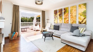 A living room with a sofa, a coffee table, and a view of a balcony with outdoor furniture.