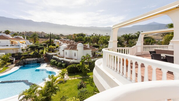 A resort with a swimming pool, lush greenery, and a view of mountains and the sea.