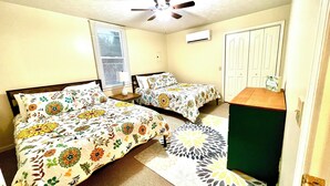 Ein Schlafzimmer mit zwei Betten, einem Deckenventilator, einer Klimaanlage und einer Tür mit einem kleinen Tisch darauf.