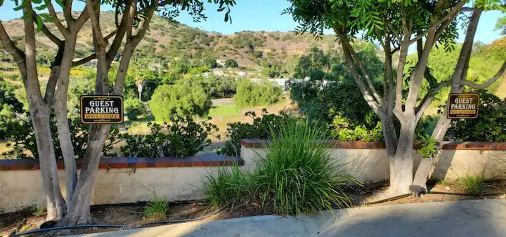 A guest parking area with signs, trees, and a view of a hilly landscape.