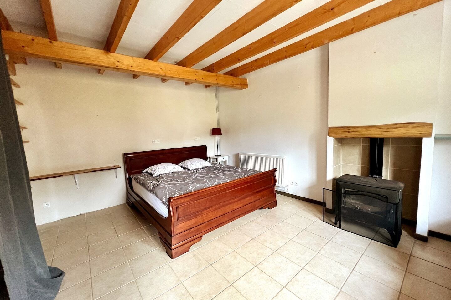 Un dormitorio con cama de madera, un pequeño calentador y suelo de baldosas.