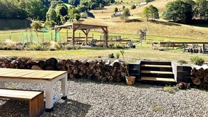 Ein rustikaler Außenbereich mit einem Holztisch und Bänken, umgeben von einer Steinmauer und einem Holzstapel.