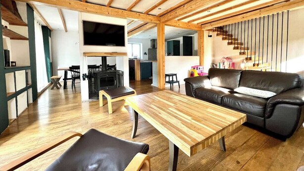Ein geräumiger Wohnbereich mit Holzboden, einem schwarzen Ledersofa, einem Holztisch und einem Esstisch mit Stühlen.