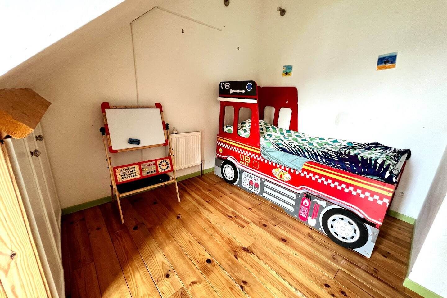 Ein Zimmer mit Holzboden, einer Tafel und einem Bett, das wie ein Feuerwehrwagen gestaltet ist.