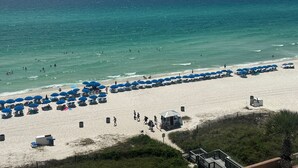 Una spiaggia con numerosi ombrelloni blu e lettini, una riva sabbiosa e l'oceano sullo sfondo.