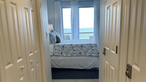 Una camera da letto con un letto, una ventola a soffitto e vista sull'oceano attraverso ampie finestre.