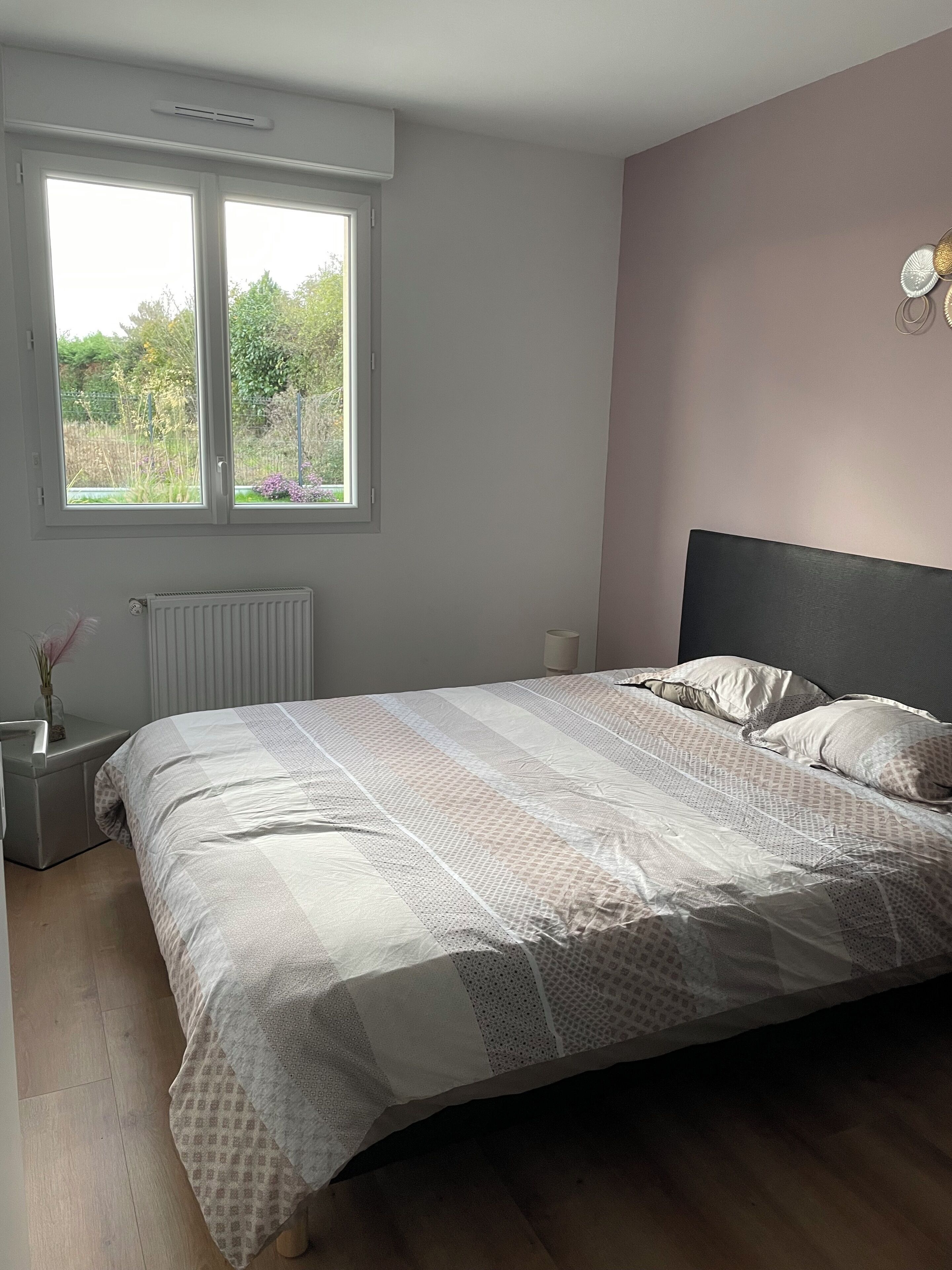 Ein Schlafzimmer mit Bett, Fenster, Heizkörper, Nachttisch und Beistelltisch.