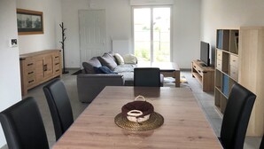 A modern living room with a dining table, chairs, a sofa, and a television. - Gîte les Coquelicots (Garennes-sur-Eure)